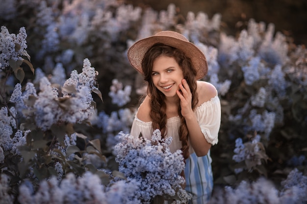 A teenage teen is a close-up of standing on background of the lilac bushes.