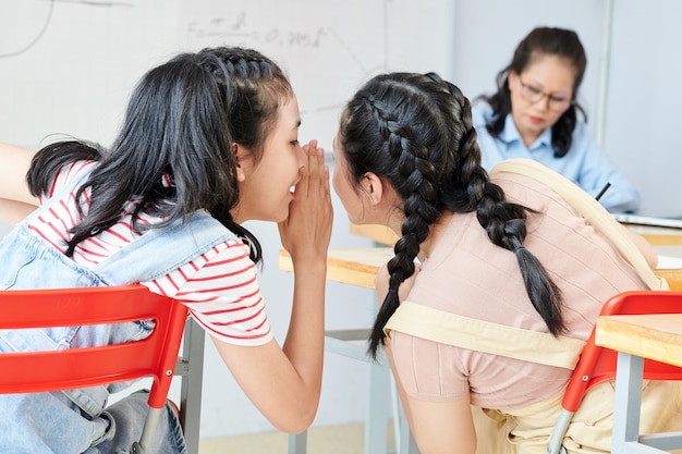 写真 彼女のクラスメートの耳に正しい答えをささやく10代のベトナムの女子高生