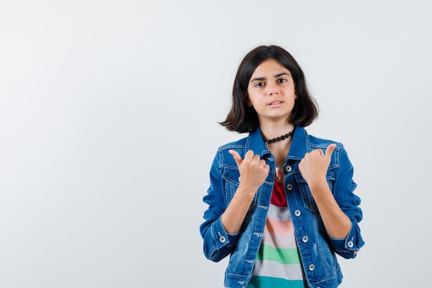 the teenage woman is pointing sideways with thumbs on white background