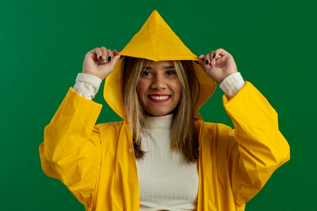 Donna adolescente in studio girato con sfondo verde in posa ed espressioni facciali che indossa un impermeabile giallo e camicetta bianca testurizzata