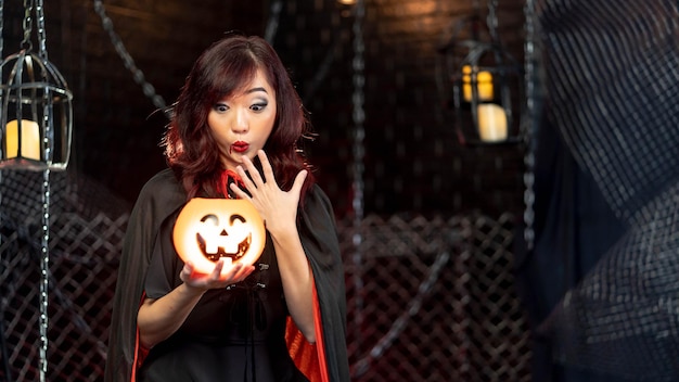 Teenage woman wearing witch costume for Halloween holding pumkin in halloween theme Emotion woo