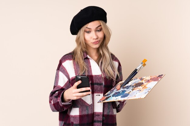 Teenager artist girl holding a palette isolated on blue