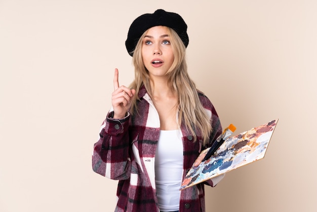 Teenager artist girl holding a palette thinking an idea pointing the finger up