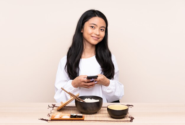 Ragazza asiatica dell'adolescente che mangia alimento asiatico isolato su beige