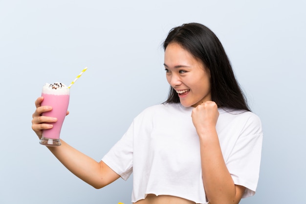 Teenager asian girl holding a strawberry milkshake celebrating a victory