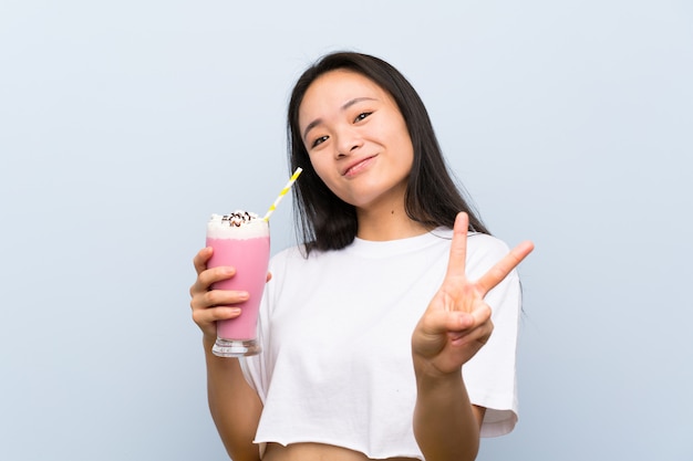 Teenager asian girl holding a strawberry milkshake smiling and showing victory sign