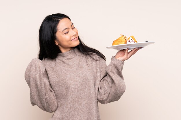 Teenager Asian girl holding waffles isolated on beige