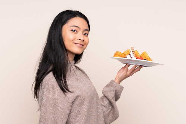 Teenager Asian girl holding waffles isolated on beige