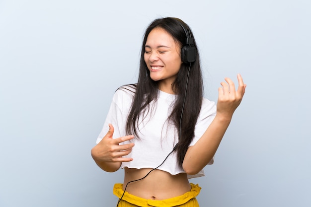 Teenager asian girl listening music over isolated blue wall