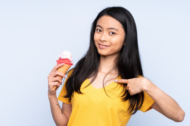 Ragazza asiatica dell'adolescente con un gelato della cornetta isolato sul blu