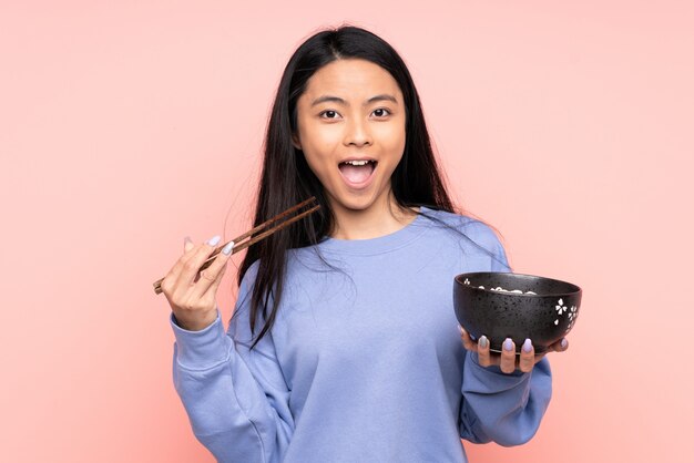 Teenager Asian woman isolated on beige background holding a bowl of noodles with chopsticks