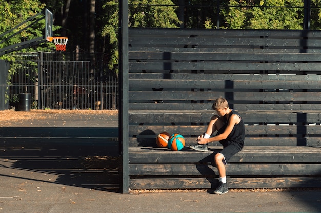 teenager basketball player sitting at sports ground tying shoelaces