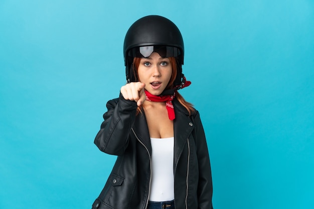 Teenager biker girl isolated on blue wall surprised and pointing front