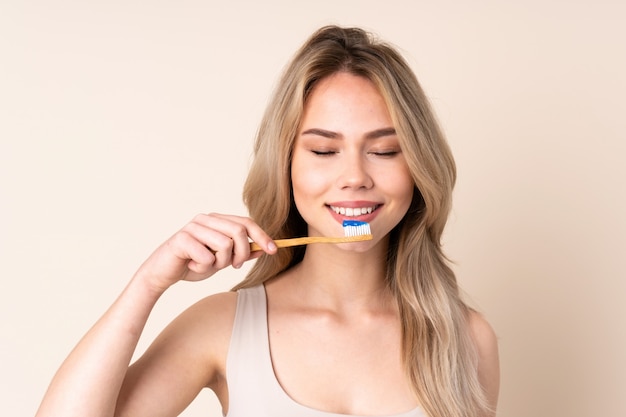 Teenager blonde girl brushing her teeth over wall