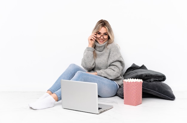 Teenager blonde girl eating popcorn while watching a movie on the laptop