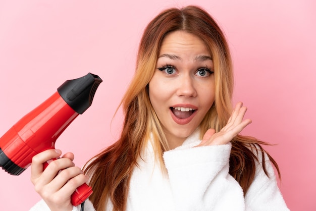 Teenager blonde girl holding a hairdryer over isolated pink background