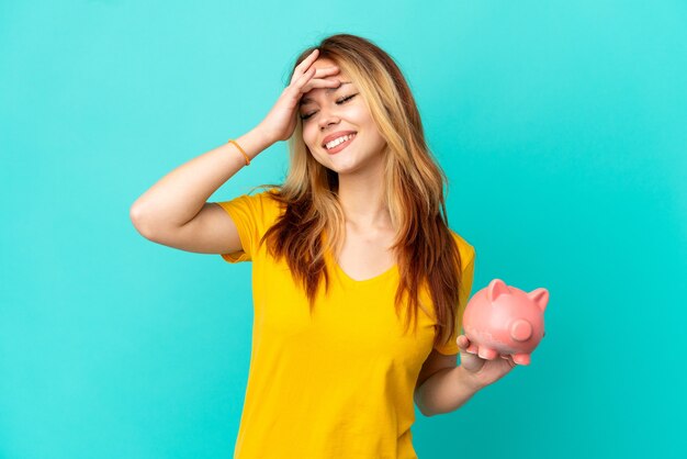 Teenager blonde girl holding a piggybank over isolated blue background smiling a lot