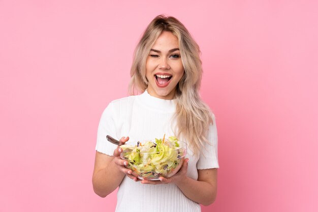 Teenager blonde girl holding a salad over pink wall