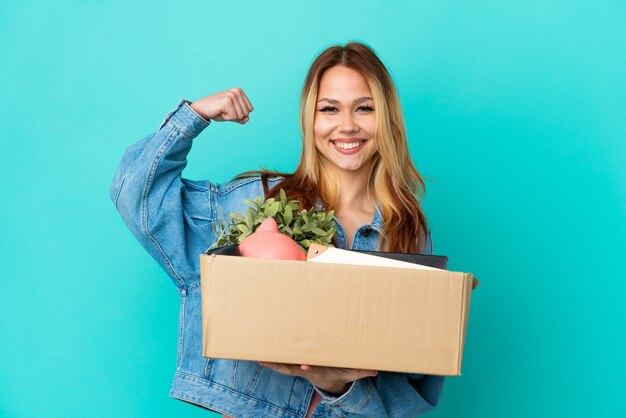 Teenager blonde girl making a move while picking up a box full of things doing strong gesture