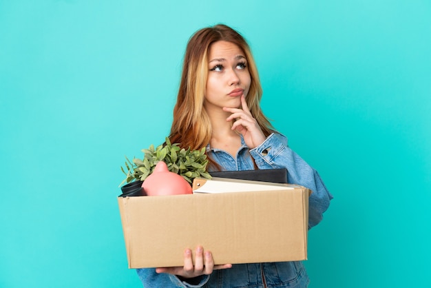 Teenager blonde girl making a move while picking up a box full of things having doubts while looking up