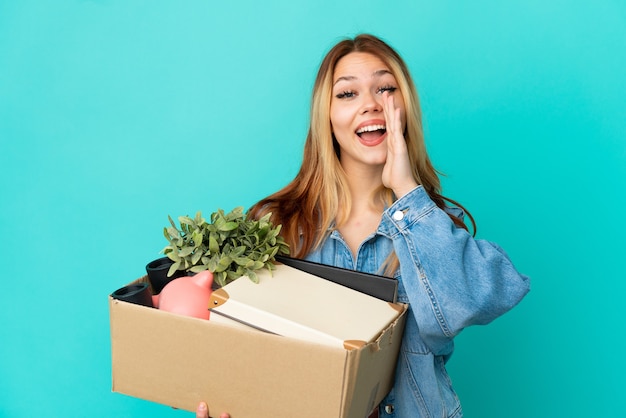 Teenager blonde girl making a move while picking up a box full of things shouting with mouth wide open