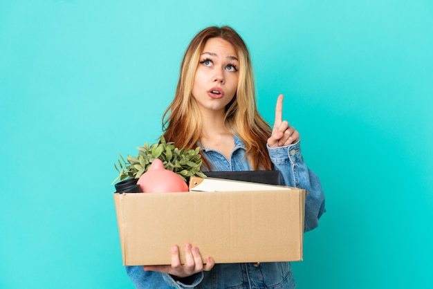 Teenager blonde girl making a move while picking up a box full of things thinking an idea pointing the finger up