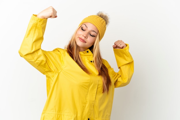 Teenager blonde girl wearing a rainproof coat over isolated white background doing strong gesture