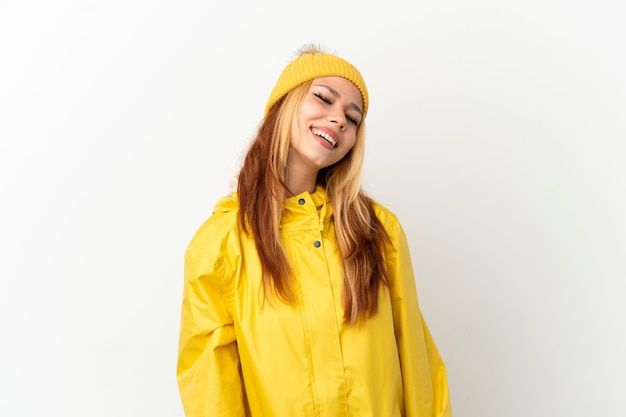 Teenager blonde girl wearing a rainproof coat over isolated white background laughing