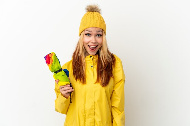 Teenager blonde girl wearing a rainproof coat over isolated white background with surprise facial expression