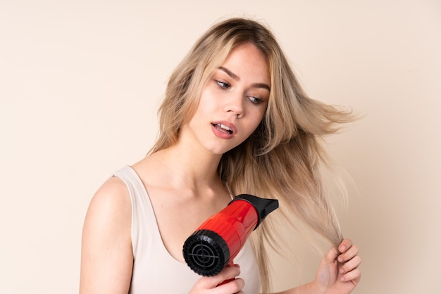 Teenager blonde girl with hairdryer over isolated