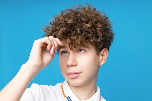 A teenager on a blue background looks at his hair