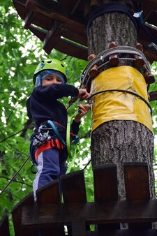 Un ragazzo adolescente sale le scale sospese da un albero all'altro in un parco divertimenti in corda