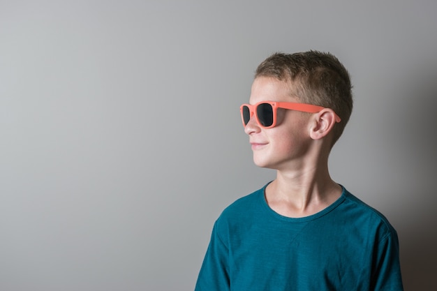 Teenager boy in coral color sunglasses and blue tshirt on bright background