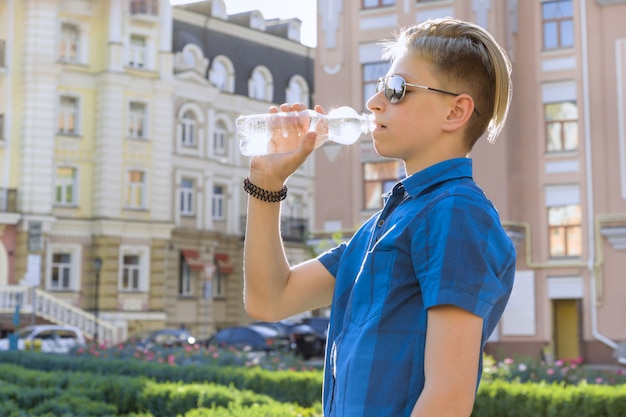 Питьевая вода мальчика подростка от бутылки на солнечный жаркий летний день в городе