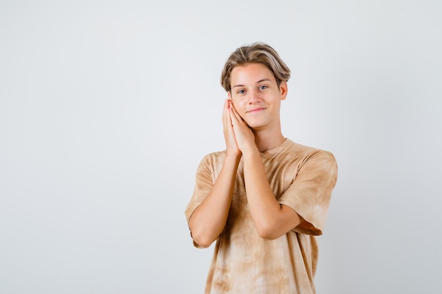 Teenager boy leaning cheek on palms as pillow in t-shirt and looking cheerful. front view.