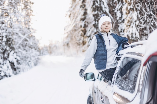 Teenager boy looking out of car window traveling in winter snowy forest Road trip adventure and local travel concept Happy child enjoying car ride Christmas winter holidays and New year vacation