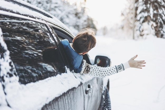 Foto ragazzo adolescente che guarda fuori dal finestrino dell'auto che viaggia nella foresta innevata d'inverno avventura di viaggio su strada e concetto di viaggio locale bambino felice che si gode il giro in macchina vacanze invernali di natale e vacanze di capodanno