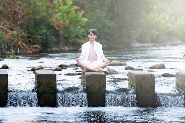 Teenager boy meditating in river