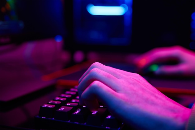 Teenager boy play computer video game in dark room use neon colored rgb mechanical keyboard workplac