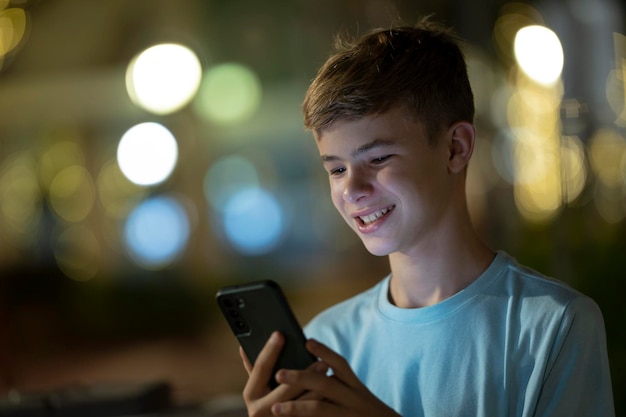 Teenager boy playing online video game with his friend on cellphone outdoors at night