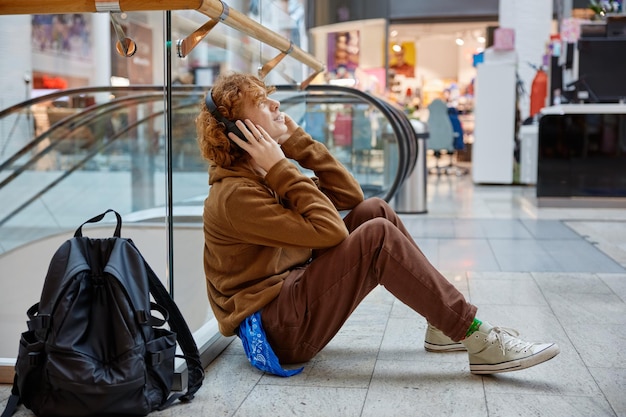 写真 ショッピングモールでリラックスしている十代の少年が ⁇ 床に座って音楽を聴いています ⁇