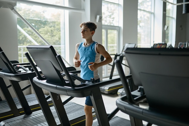 Photo teenager boy running doing cardio exercise on treadmill machine at sports gym. childhood, strength training and fitness concept