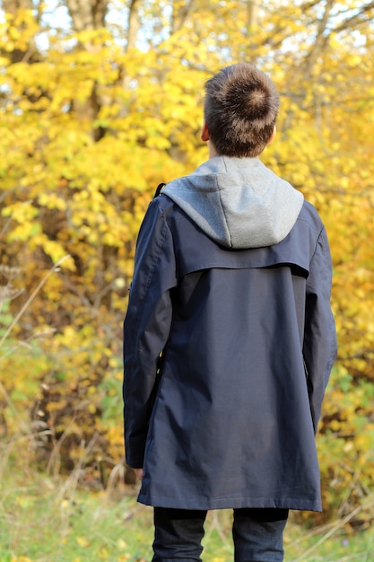 Teenager boy stands with his back in the autumn forest