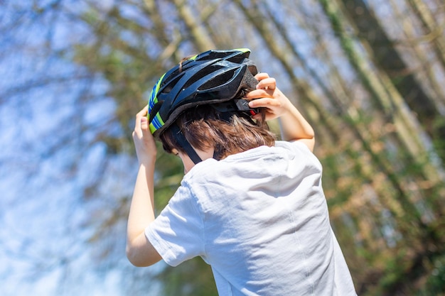 Teenager boy in a white t-shirt putting on himself a safety velo helmet, back view, copy space. Children activities outdoor concept. safe sports and hobbies.