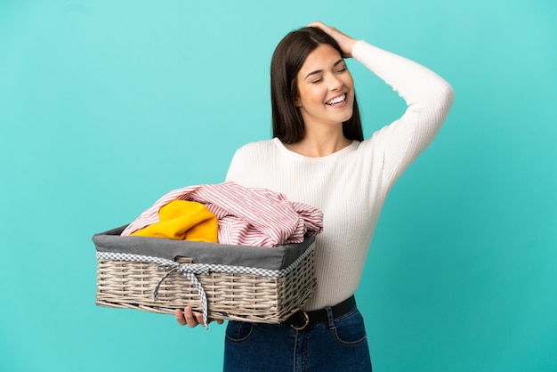 Teenager Brazilian girl holding a clothes basket isolated on blue background smiling a lot