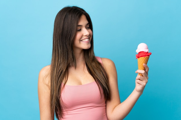 Teenager Brazilian girl holding a cornet ice cream over isolated blue background with happy expression