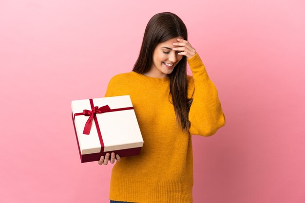 Teenager Brazilian girl holding a gift over isolated pink background laughing