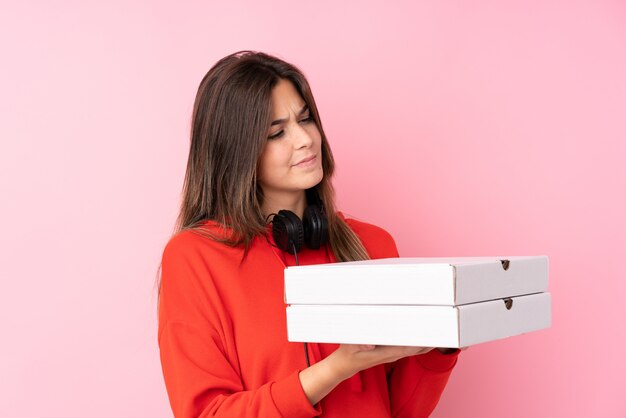 Teenager Brazilian girl holding pizza boxes over isolated pink wall with sad expression