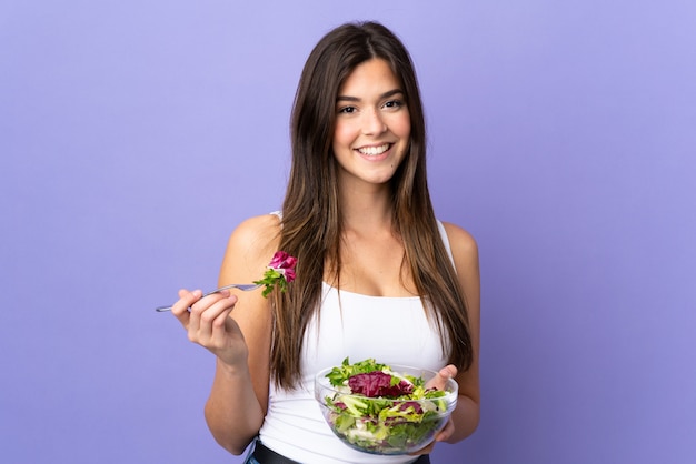 Teenager Brazilian girl holding a salad over isolated purple background