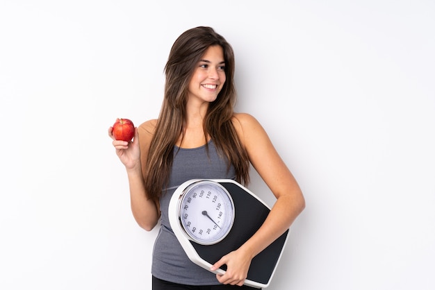 Teenager Brazilian girl holding a scale with weighing machine and with an apple